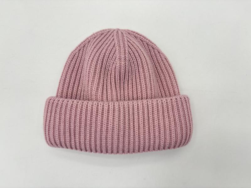 Bonnet hivernal rose poudré côtelé avec revers replié posé à plat sur fond blanc texture tricot