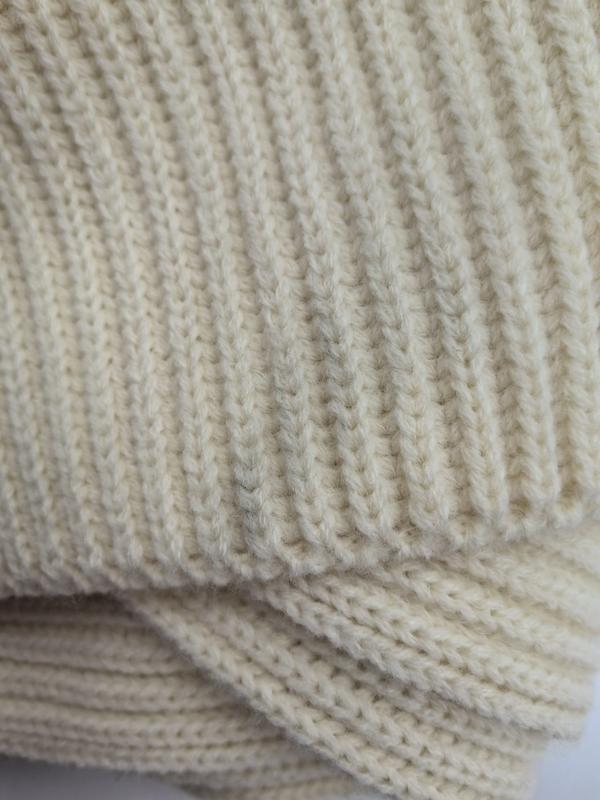 Gros plan sur plaid grosse maille crème ivoire aux rangées côtelées épaisses et couches repliées révélant la texture laine