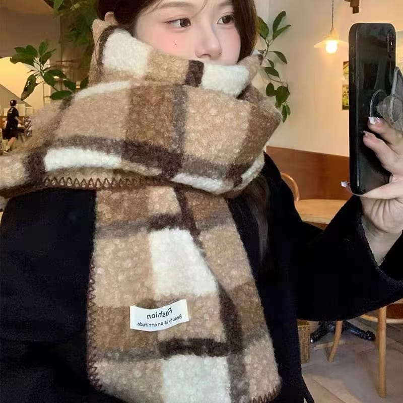 Jeune femme portant écharpe épaisse floue carreaux beige marron crème se prenant en selfie ambiance intérieure
