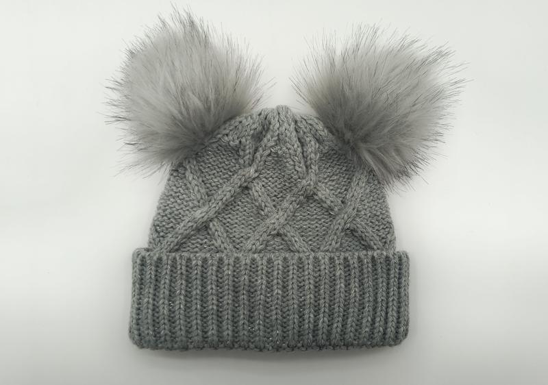 Bonnet hivernal gris en maille torsadée avec deux gros pompons fourrure synthétique sur le dessus et revers côtelé