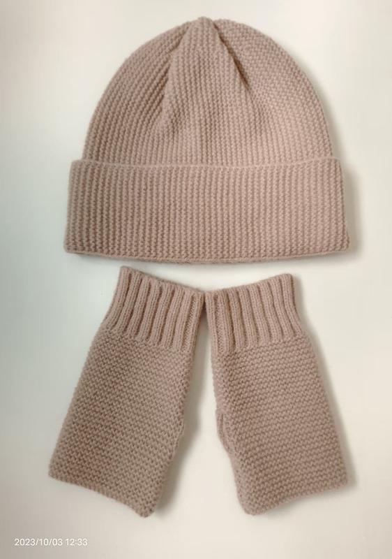 Bonnet et mitaines sans doigts en grosse maille rose poudré posés à plat fond blanc