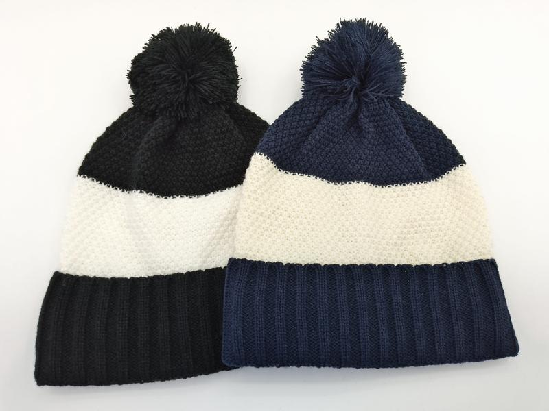 Deux bonnets pompon bicolores tricot épais posés à plat