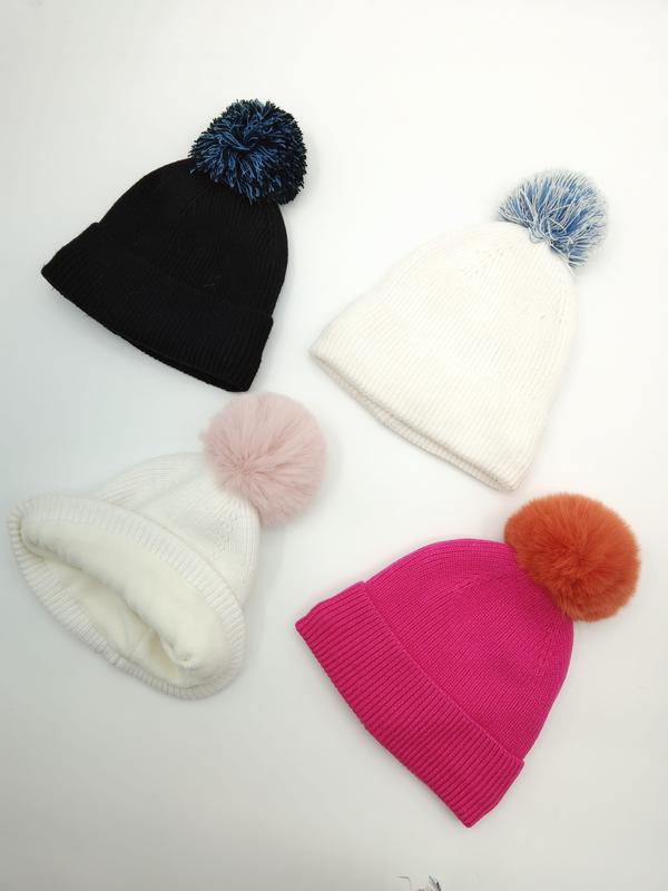 Quatre bonnets tricotés côtelés à pompons colorés noir blanc et rose fuchsia posés à plat