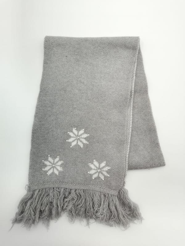 Plaid tricoté gris replié avec motifs flocons de neige blancs en jacquard et franges décoratives