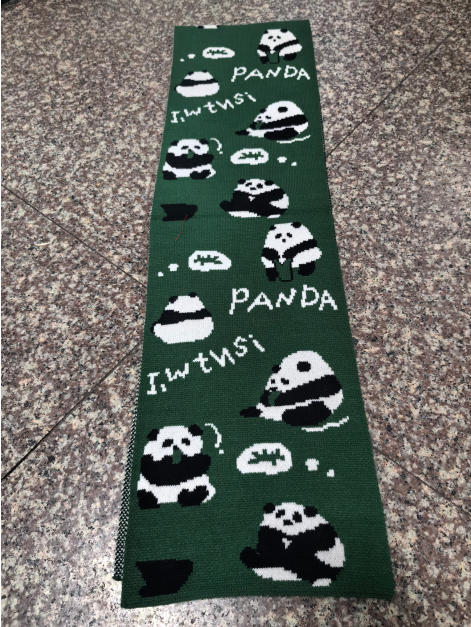 Écharpe tricotée verte avec illustrations panda noir et blanc répétées et inscription PANDA posée à plat sur carrelage