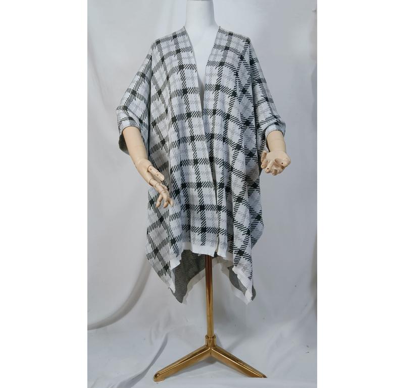 Mannequin portant un poncho cape tricot carreaux noir et blanc ouvert devant avec ourlet asymétrique sur trépied doré