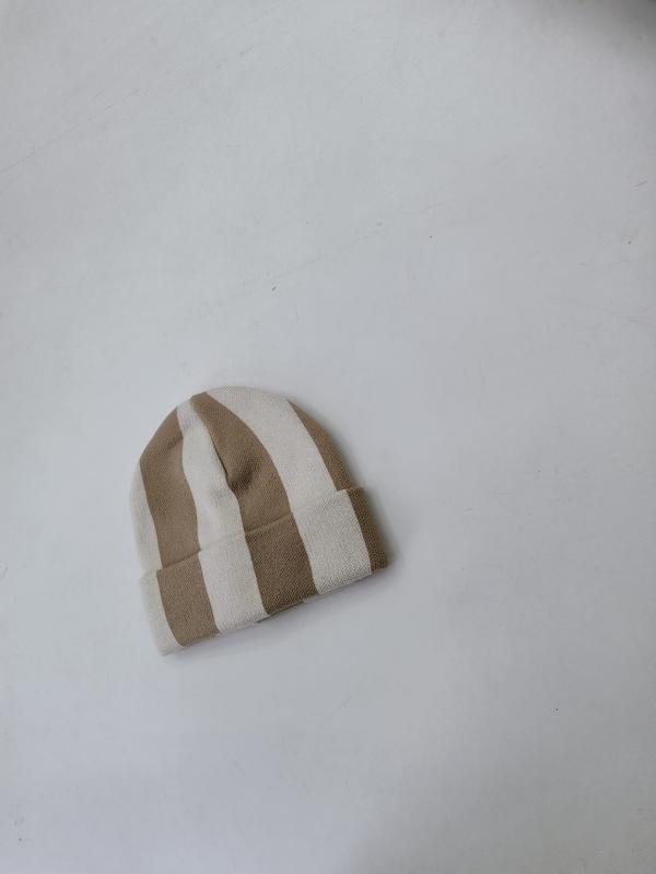 Petit bonnet tricoté rayures larges camel et crème posé à plat sur surface blanche