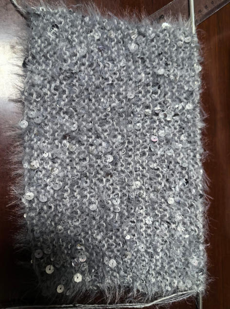 Gros plan tissu tricoté gris moelleux avec paillettes argentées dispersées sur surface en bois – matière écharpe hiver brillante