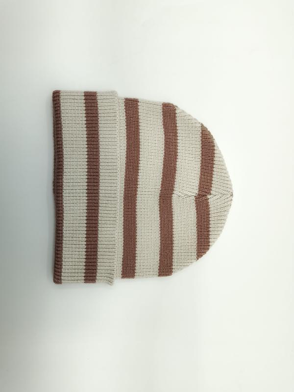 Bonnet tricoté côtelé à rayures crème et marron posé à plat sur fond blanc