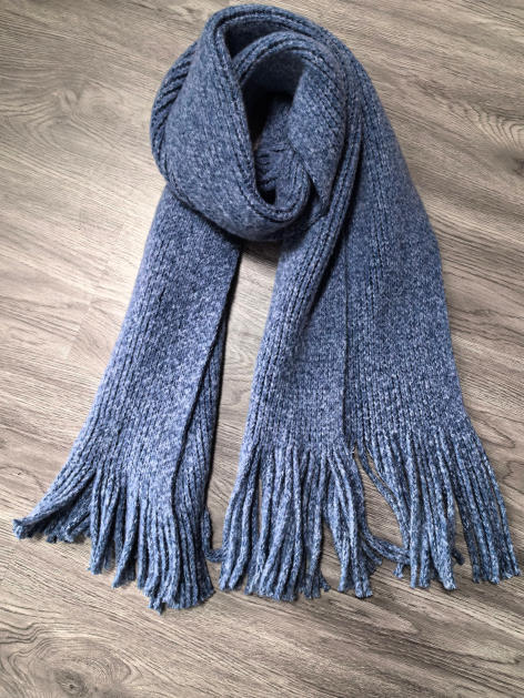 Longue écharpe grosse maille gris chiné avec franges aux extrémités pliée sur parquet bois – accessoire hiver